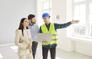 Profesyonel müteahhit, ev yenileme projesini dizüstü bilgisayar ve planla tartışmak için olumlu bir karı ve kocayla işbirliği yaparak, inşaat planlama ve takım çalışmasını vurguladı.