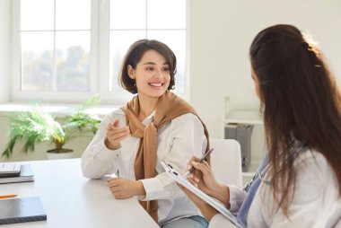 Klinik ziyareti sırasında kadın doktor hastayla konuşuyor, reçeteyi, tıbbi muayeneyi, muayene sonucunu, muayeneyi, pratisyeni ziyaret eden kızı anlatıyor, not tutuyor.