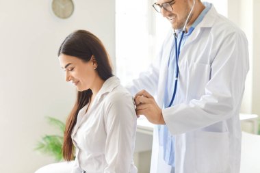 Doktor ya da hemşire, klinikteki kadın bir hastanın akciğerlerini ve nefesini incelemek için steteskop kullanarak sağlık kontrolü yapar. Sağlık desteği ve rutin muayene sağlanması.