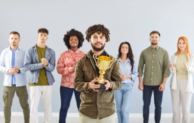 İş hayatında başarı ödülünü elinde tutan kendine güvenen genç bir adamın portresi çeşitli insanlardan oluşan bir ekiple birlikte şirketteki en iyi çalışan ödülünü alkışlıyor..