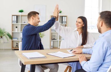 Ofiste danışmanla gayrimenkul satın aldıktan sonra birkaç müşteri beşlik çakarak bir anlaşmayı kutluyor. Kazançlı bir yatırımdan duyulan memnuniyet ve heyecanı yansıtıyor..