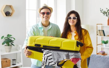 Turist yaz insanları seyahat, tatil için bavul hazırlarken mutlu olurlar, büyük sarı bavula bir şeyler koyarlar, balayı planlarlar, rüya görürler, parlak yaz tatili plaj kıyafetleri giyerler.