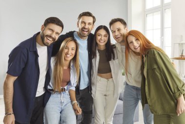 Mutlu gülümseyen bir grup genç arkadaş ya da günlük giysiler içinde neşeli ve kapalı mekanlarda kameraya olumlu bakan meslektaşlar. Neşeli erkek ve kadınların portresi yan yana duruyor..