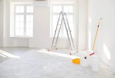Basamaklı merdiven, yeni evdeki boş ışık odasında duran boya silindirli kovalar ya da yeni boyanmış beyaz duvarları olan bir daire. Evdeki yenileme işlemi. Ev onarımı ve taşınma günü konsepti.