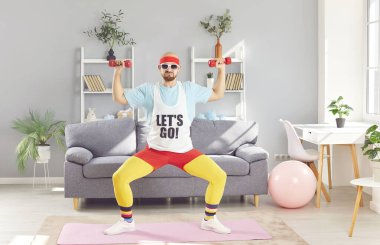 Komik kıyafetli, güneş gözlüklü ciddi kel bir adam ev spor salonunda dambıl egzersizi ve çömelme hareketleri yapıyor. Fitness eğitimi ve antrenman rutini mizah ve spora bağlılığın bir karışımını gösteriyor..