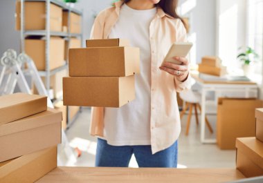 Küçük depo arkaplan üzerinde KME sahibi lojistik denetleyici paketlenmiş kutular tutmak cep telefonu iletişim mesajı ileti istemcisi tarama bar kod barkod izleme durumu Veri ağ sistemi postası