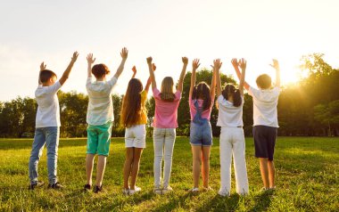 Parktaki çocuklar. Yeşil parkta sıra sıra beklerken bir grup çocuk el kaldırsın. Güneş ışınlarına uzanan gündelik giysiler içindeki erkek ve kızların arka plan görüntüsü. Çocukluk kavramı.
