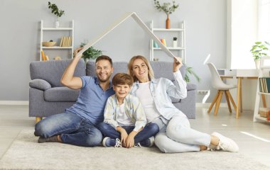 Mutlu, gülümseyen bir ailenin portresi. Küçük çocukları evde oturmuş, ev çatısı yapıyor ve kameraya bakıyor. Sigorta, ipotek, güvenlik ve koruma kavramı.