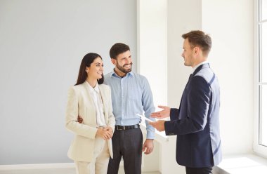 Aile çifti ve erkek emlakçı yeni bir oda gösteriyor, emlak teklifi yapıyor. Satın alma sözleşmesi ya da kira sözleşmesi sunuyor, müşterilerin ofislerini gözetliyor, yeni sözleşme görüşmeleri yapıyor, kiracı ev sahibi