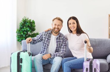 Mutlu aile çifti kanepeye oturmuş bavullarını hazırlayıp yaz yolculuğuna hazırlanıyorlar. Gülümseyen karı koca, yaklaşan macera için heyecanlanıyor. Seyahat ve tatil.