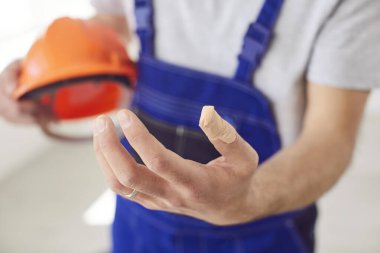 İş kazasından sonra kaskı tutan üniformalı erkek işçiyi yakın çekiyoruz. İnşaat alanında eli bandajlı bir şekilde duruyor. Güvenlik, sakatlık ve ilk yardım kavramı.
