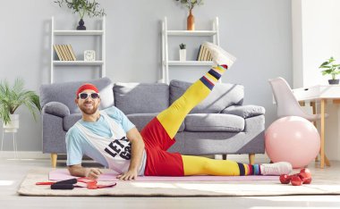 Renkli spor kıyafetleriyle evde spor yapan komik bir adam. Gülümseyen sakallı adam oturma odasında aerobik yapıyor. Konsept fiziksel egzersiz, sporcu, sağlıklı yaşam tarzı, süpermen egzersizi