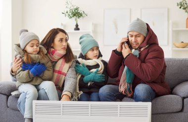 Soğuk kış odasında sinirli bir aile, hoşnutsuz ebeveynler, ısıtıcının yanında çocuklar, üst katta oturan kiracı, apartman yöneticiliğini arayıp düşük sıcaklıktan şikayet eden kiracılar.