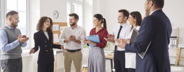 Toplantı odasında duran bir grup şirket çalışanının iş projesi ve şirket finansmanı büyümesinden bahseden genç bir kadın. Ofisteki bir konferansta kadın konuşmacıyı alkışlayan iş adamları