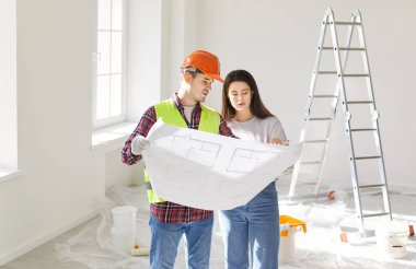 Foreman, yeni dairesinin tasarım projesinin genç ev sahibine boş bir odada duran taslağı gösteriyor. İç dekorasyon için erkek müteahhitle buluşacağım. Taşınma konsepti.