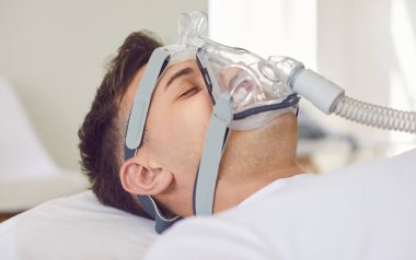 Tıbbi yüz maskesi takan hasta, gözleri kapalı oksijen maskesi, ciğerleri için oksijen gazı soluyan, havalandırma sağlık desteği, koronavirüs hastalığından kaynaklanan yapay akciğer havalandırması, korona virüsü zatürresi.