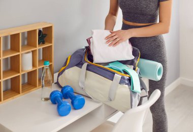 Genç bir sporcu antrenman için çantasını evde topluyor, yakın plan. Spor kıyafetli bir kadın çantasına havlu koyuyor. Sağlıklı yaşam tarzı, atletik vücut, sporcu, atlet bavulu