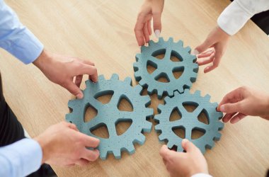 Vites tekerlerini tutan iş adamlarının el yapımı görüntülerini yakın planda tut ve birleştir. Ofis çalışanları ofis masasına dişli dişli yerleştiriyor. İyi takım çalışması, işbirliği, ortaklık. Üst görünüm.