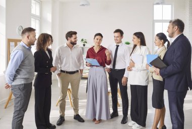 Bir grup meslektaş, ofiste bir iş toplantısı veya sunum sırasında sohbet eder. Ekip, profesyonel hedeflere ulaşmak için insanlar arasındaki takım çalışmasını ve işbirliğini vurguluyor.
