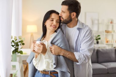 Evdeki oturma odasında bir bardak içecekle bekleyen neşeli genç adam ve kadının portresi. Aşık mutlu bir çift. İlişkiler, romantizm ve Sevgililer Günü konsepti.