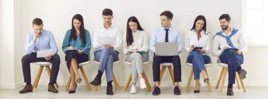 Koltuklarda oturan genç iş adamları özgeçmişleri ve dizüstü bilgisayarlarıyla toplantı ya da konferansa hazırlanıyor. İş başvurusunda bulunan adaylar görüşme daveti için bekliyorlar. Pankart.