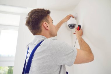 Genç erkek teknisyen, güvenlik kameralarını beyaz bir tornavidayla içeri yerleştiriyor. Modern ofiste ya da evde güvenlik kamerası tamir eden bir işçi. Güvenlik ve güvenlik kavramı