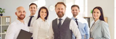 Ofisteki çeşitli tatmin olmuş bir iş ekibinin grup portresi gülümseyerek kameraya bakıyor. İş yerinde takım çalışmasının önemini vurgulayan bir topluluk..