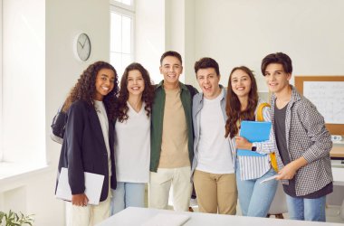 Sınıfta kameraya bakan mutlu, gülümseyen lise öğrencilerinin portresi. Dost canlısı erkekler ve kızlar içeride sırada bekliyorlar. Eğitim ve okul konseptine dönüş.