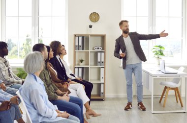 Profesyonel işletme koçu farklı seyirciler için bir sunum yapıyor. Ofisteki bir toplantıda şirket çalışanlarıyla tecrübelerini paylaşan genç bir adam.