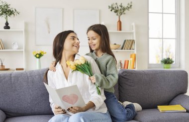 Sevgi dolu küçük bir kız çocuğu mutlu anneyi çiçek buketi ve Kadınlar Günü 'nde ya da Anneler Günü' nde evde bir kartpostal hediyesiyle şaşırtır. Aile sevgisi, sevgi ve özel bir bayram kutlaması..