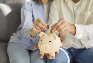 Kanepede oturan, kumbaralarını elinde tutan, bütçelerini birlikte planlayan genç bir aile fotoğrafı. Kadın ve erkek para kutusuna para koyuyor, aile ekonomisini yönetiyor ve gelecek için para biriktiriyor..