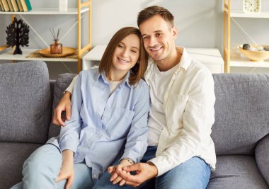 Evdeki oturma odasındaki kanepede el ele tutuşan evli çiftin portresi. Gülümseyen aile babası ve kadın kanepede dinleniyor. Aşk ve uyum ilişkileri kavramı.