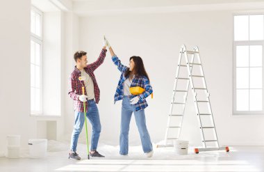 Olumlu çift yeni evin yenilenmesi sırasında işbirliği yaparak duvar boyarken beşlik çakıyor. Takım çalışması ve işbirliği, inşaat görevlerinde ortak bir çabayı yansıtıyor.
