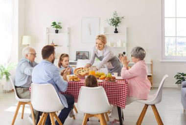 Mutlu anne büyük ailesi için festival masasına pizza getiriyor. Ebeveynler, büyük ebeveynler ve iki küçük çocuk bayram kutlamaları sırasında evde toplanıp yemek yiyorlar..