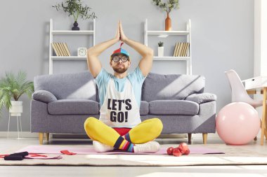Komik adam yoga egzersizi sırasında evde meditasyon yapıyor. Spor salonunda rahatlık ve farkındalığı birleştiren bir antrenmana katılırken sağlığına ve sağlığına odaklanıyor..