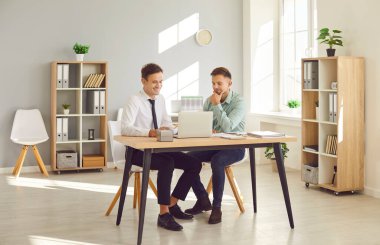 İki neşeli, güler yüzlü iş adamı şirket çalışanı iş yerindeki mali belgelerle masada oturuyor ve dizüstü bilgisayar ekranına bakıyor. Muhasebeci iş konsepti.