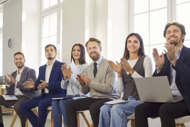 Bir grup iş adamı ofiste toplanarak, bir toplantı veya etkinlik sırasında başarıyı alkışlayarak kutluyor. Bu an takım çalışmasını, çeşitliliği ve paylaşılan başarıların neşesini vurguluyor.