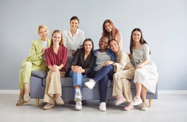 Bir grup mutlu, genç, güzel, gülümseyen Kafkasyalı, Afro-Amerikalı ve Asyalı kadın arkadaşlar gri stüdyo duvarında, kanepede oturuyorlar. Kadın topluluğu, arkadaşlık kavramı