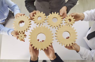 İş adamlarının vites tekerleklerini tuttukları ve birlikte katıldıkları en iyi manzara. Şirket çalışanları ofis masasının üstüne ahşap dişliler yığıyor. Ortaklık, takım çalışması ve işbirliği kavramı.