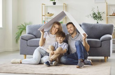 Çocuklu mutlu bir aile, ellerinde kartondan bir çatıyla evde oturuyor. Aşkı, korumayı ve yeni bir evin hayalini sembolize ediyorlar. Neşeli bir aile anı yaratıyorlar..