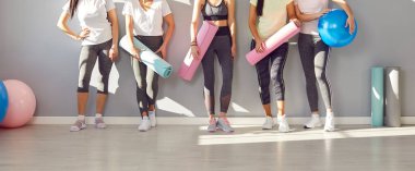 Spor kıyafetleri giymiş, spor giyinen kadınların spor salonunda yoga minderlerini tutarken ve topları ellere sığdırırken çekilmiş bir fotoğraf. Spor antrenmanından sonra içeride duran sportif kızlar. Sağlıklı yaşam tarzı kavramı.