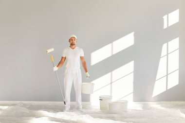 Odaklanmış ve profesyonel bir adam, silindirli ve kovalı bir dairede boyacı, yenileme sürecine dalmış. İnşaattaki uzmanlığı ve kusursuz fırça darbeleri duvarları değiştiriyor..