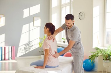 Genç doktor osteopat ya da fizyoterapist modern rehabilitasyon kliniğinde sırt ağrısını tedavi eden kadın hastaya yardım ediyor. Fizyoterapi ve fizik tedavi konsepti.