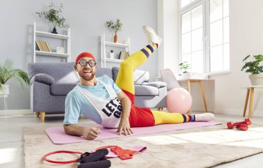 Rahat bir evde spor yaparken esneme hareketleri yapan komik bir adamın pozitif portresi. Egzersiz rutini spor ve esneklik eğitimini ev jimnastiğinin rahatlığında birleştiriyor..