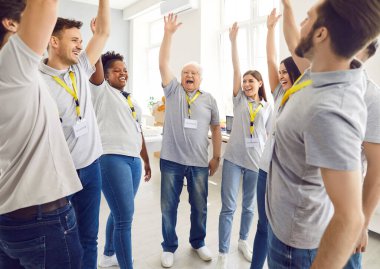 Çeşitli genç ve olgun gönüllüler el ele tutuşup toplum yardım merkezinde çalışırken mutlu mesut gülümsüyorlar. Gönüllü ve insani yardım kavramı.