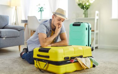 Mutlu gülümseyen adam evinde bavulunu toplayarak oturmuş internetten bilet ayırtan tablet ekran biletlerine bakıyor. Genç adam tatil gezisine hazırlanıyor. Tatil kavramı.