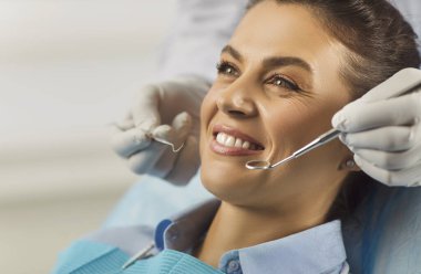 Modern diş hekimliği kliniğindeki kadın hasta portresi. Sağlık merkezindeki sağlık kontrolü sırasında. Dişçi, dişçi aletleriyle genç kadın dişlerini inceliyor. Diş sağlığı hizmetleri.