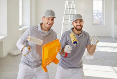 Boya rulosu tutan ve yeni dairenin duvarını boyarken eğlenen mutlu profesyonel boyacılar takımı. Tamirat yapan müteahhitler taşınmaya hazırlanıyor. Konsept yenileniyor.