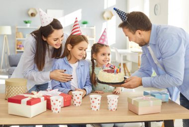 Mutlu aile parti şapkası takıyor, doğum gününü evde kutluyor, neşeli atmosferin tadını çıkarıyor. Neşeli anne ve oğul, gülümseyen babayı izliyor. Heyecanlı küçük kızına mumlarla pasta sunuyor..