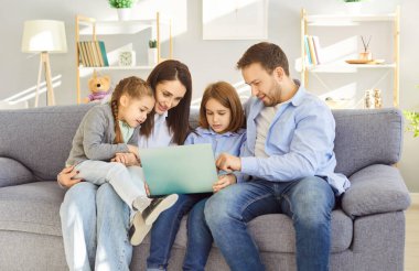 Mutlu anne, baba ve iki çocuk evde boş vakitlerini bir kanepede geçiriyorlar. İnternette dizüstü bilgisayar kullanarak eğleniyorlar. İnternette aile bağı, rahatlama ve dijital eğlence.